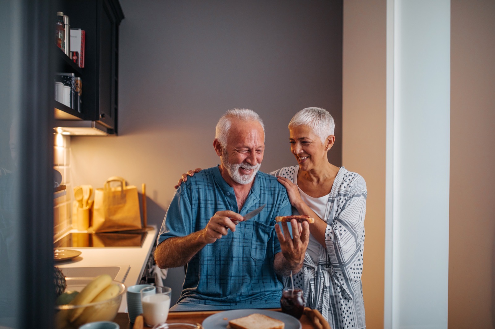 Un couple de seniors rit en préparant le petit-déjeuner dans une cuisine baignée de lumière